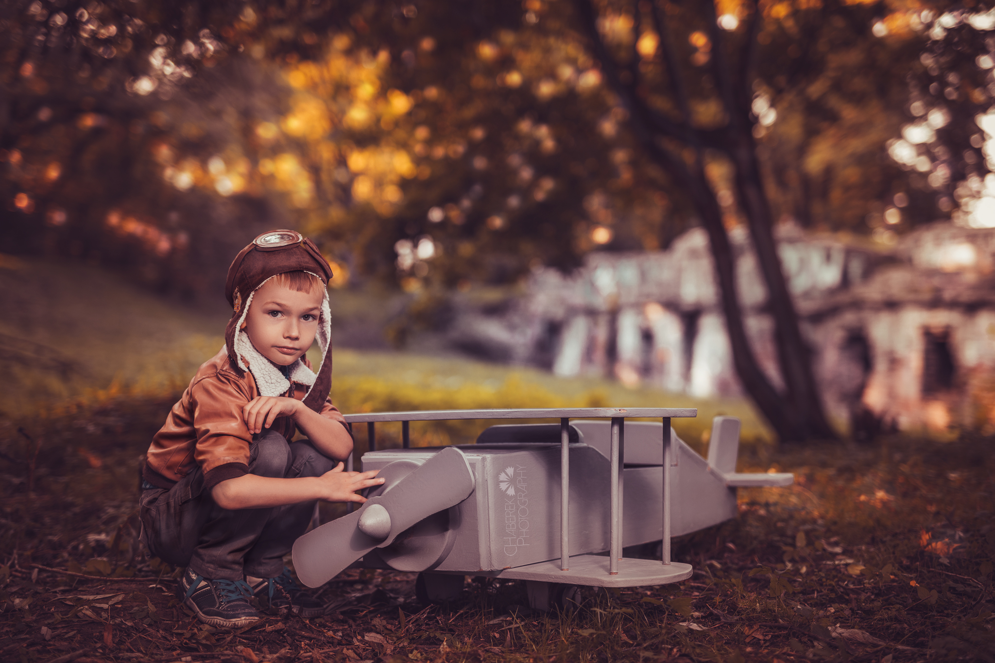 Zdjęcie ze stylizowanej tematycznej sesji zdjęciowej plenerowej z samolotem przedstawiające chłopca naprawiającego śmigło