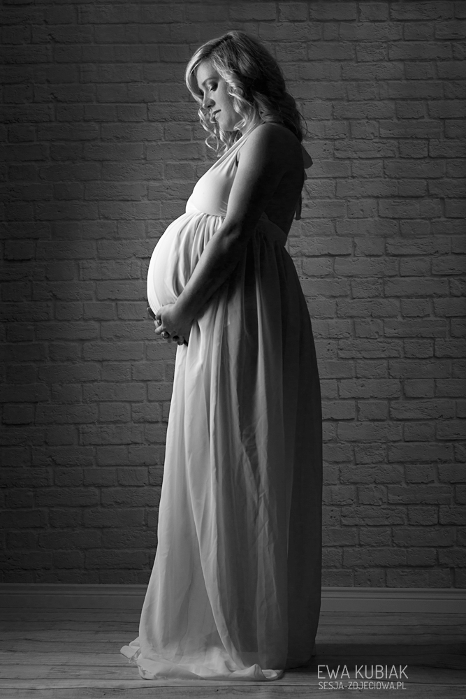 kobieta w ciąży w białej sukni podtrzymuje brzuch czarno białe zdjęcie