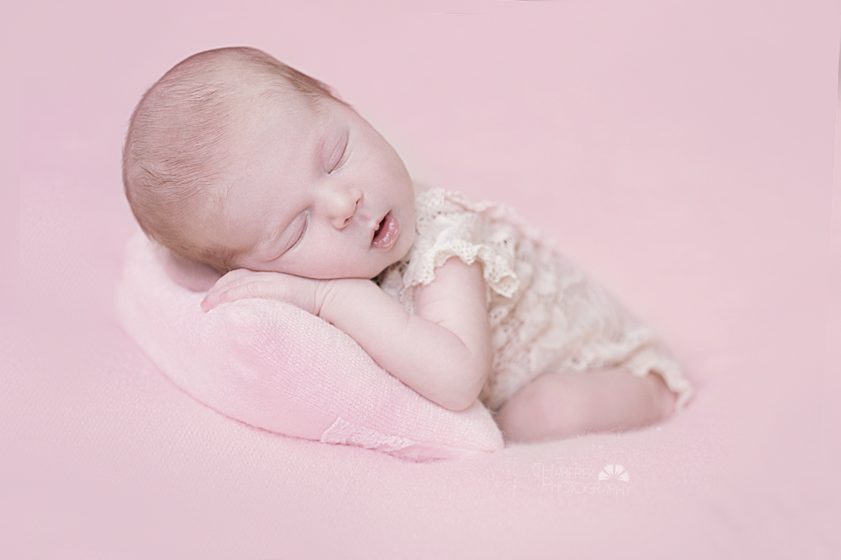 kilkudniowe dziecko na różowym tle śpiące na poduszeczce